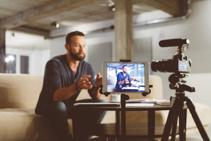 A young man talking on video interview, sitting at a desk with camera setup. 