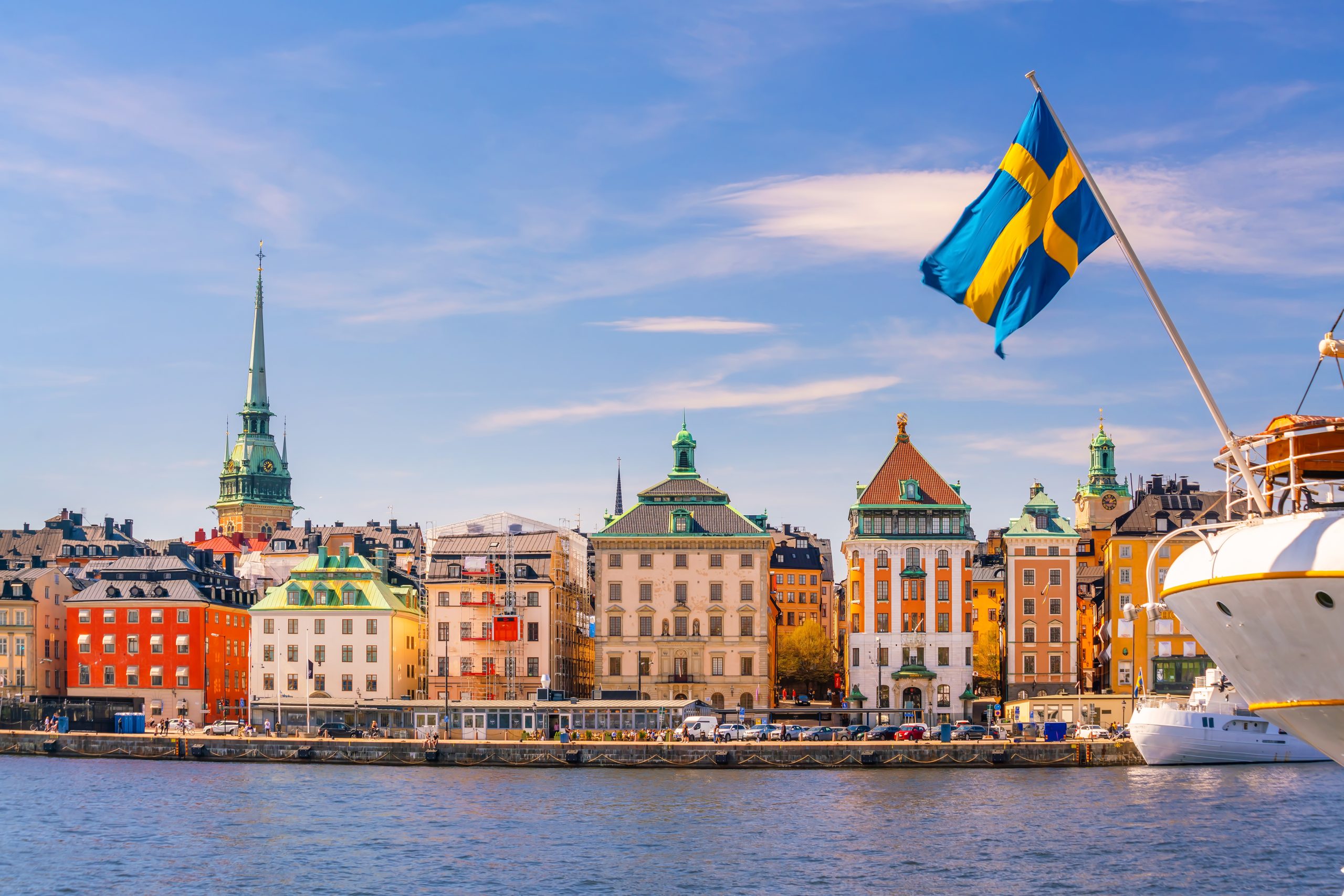 A view of Stockholm with a ship sailing and the Swedish flag waving in the foreground